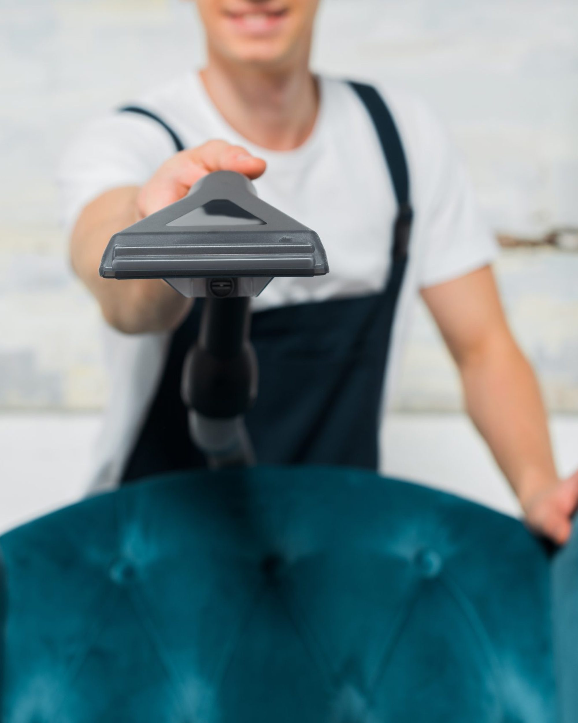 selective focus of vacuum cleaner in hand of young cleaner near modern armchair